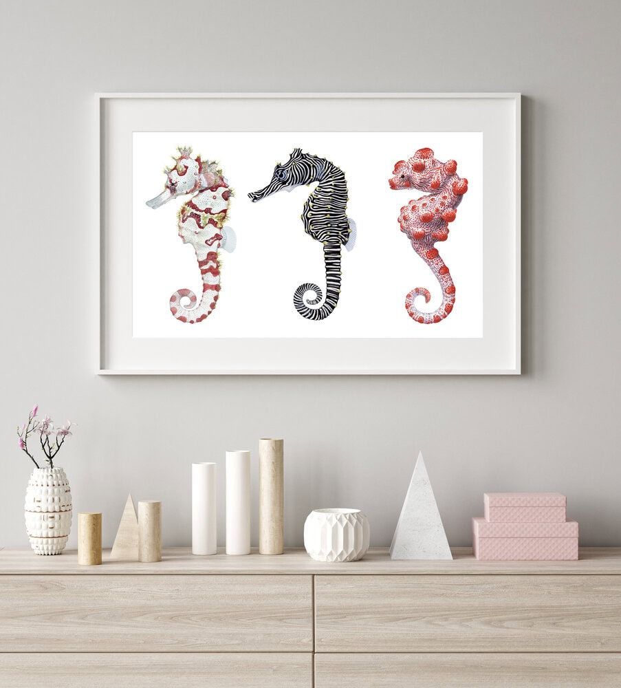 Framed artwork of three seahorses on a wall above a wooden shelf with decorative items.